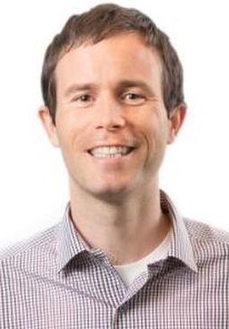 professor wearing a blue button up shirt in front of a white backdrop